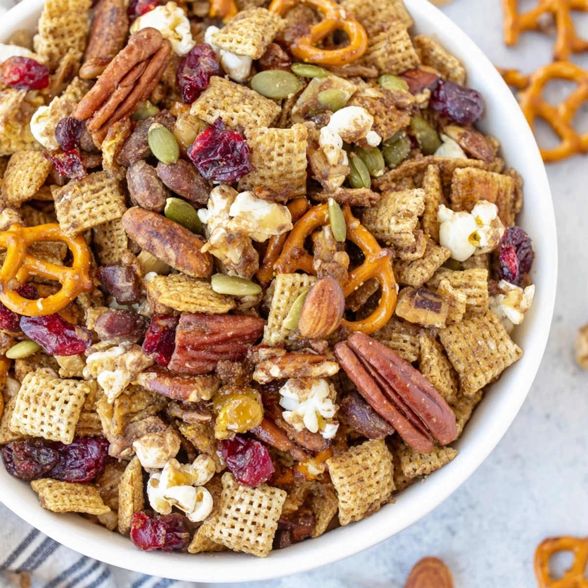 Close-up of Winter Snack Mix with cinnamon-coated cereals, pretzels, and pecans, alongside a steaming mug of hot cocoa.