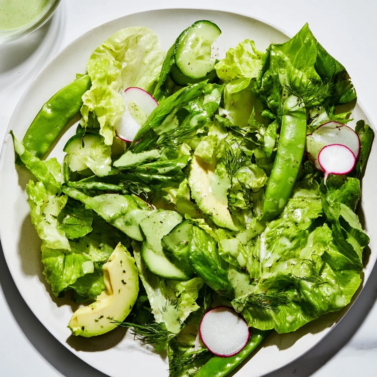 A close-up of a vibrant Green Salad with Green Goddess Dressing, featuring creamy avocado, crisp cucumber, and fresh herbs on mixed greens.  