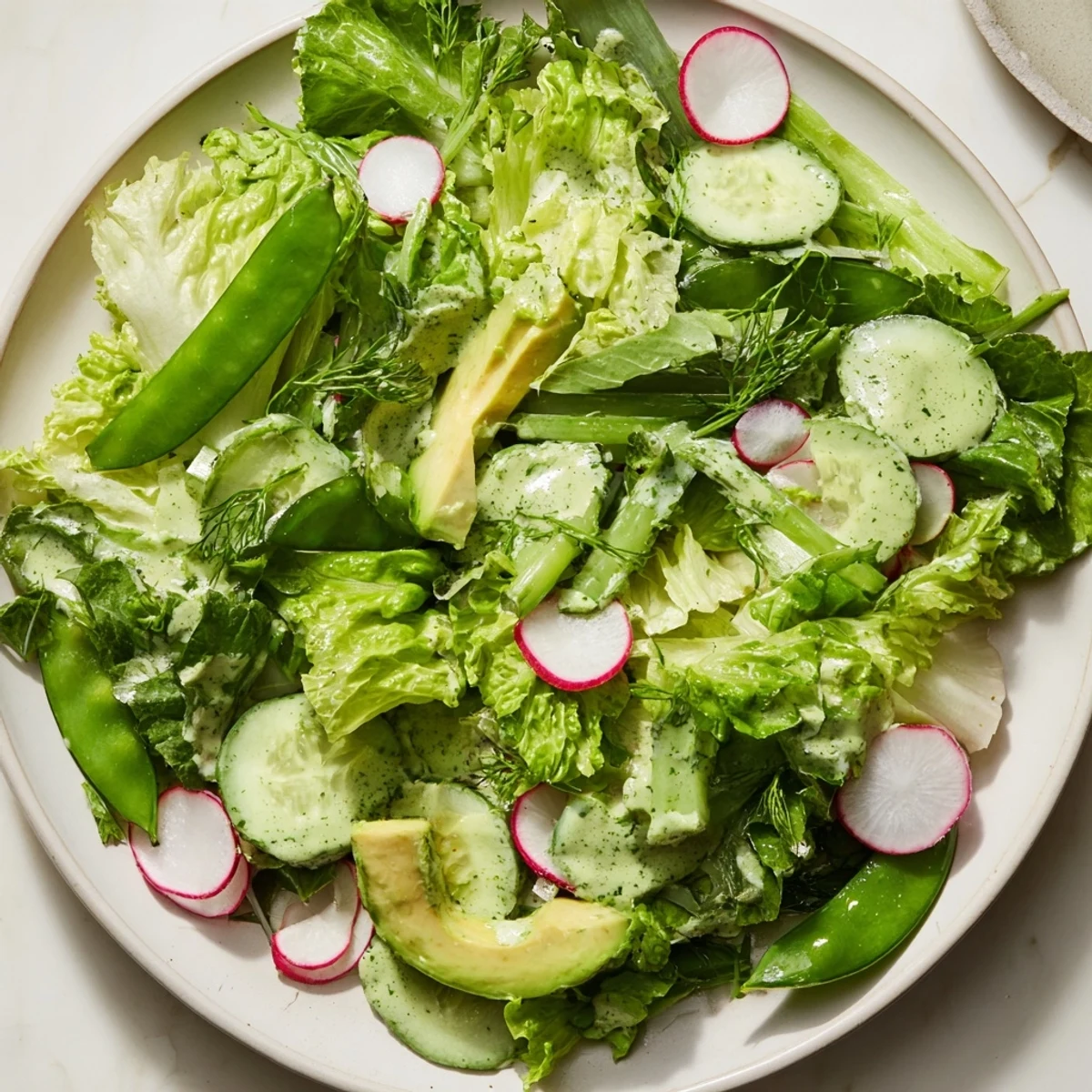 A large serving bowl of Green Salad with Green Goddess Dressing, topped with sliced radishes and sugar snap peas, ready for a light meal.  