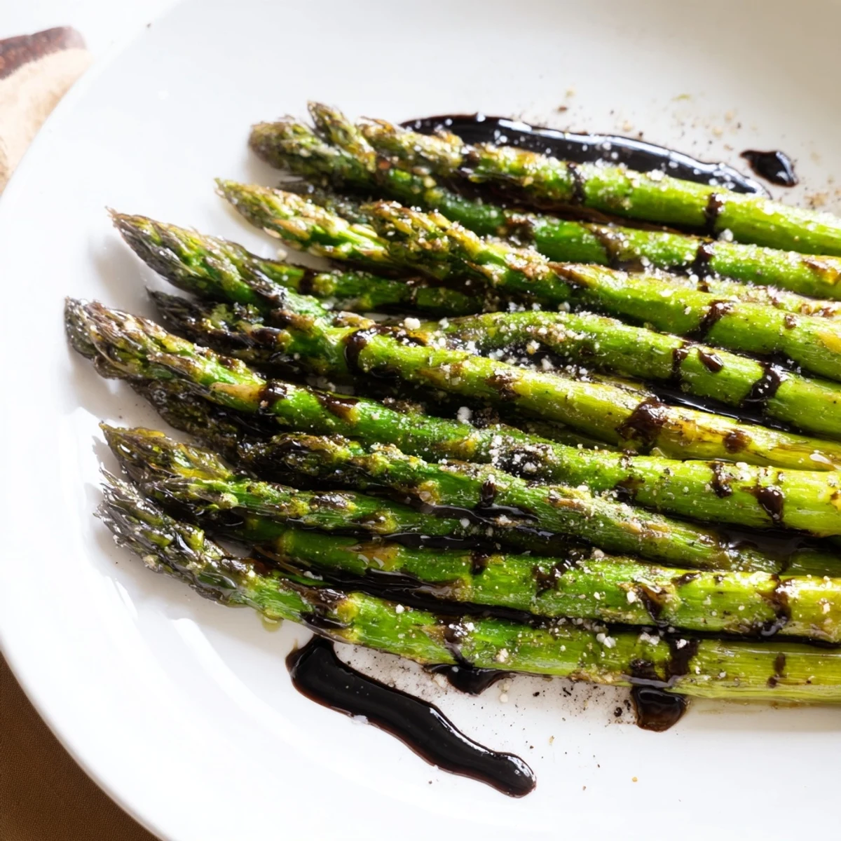 Fresh roasted asparagus with balsamic reduction glistens on a white plate, ready to serve.