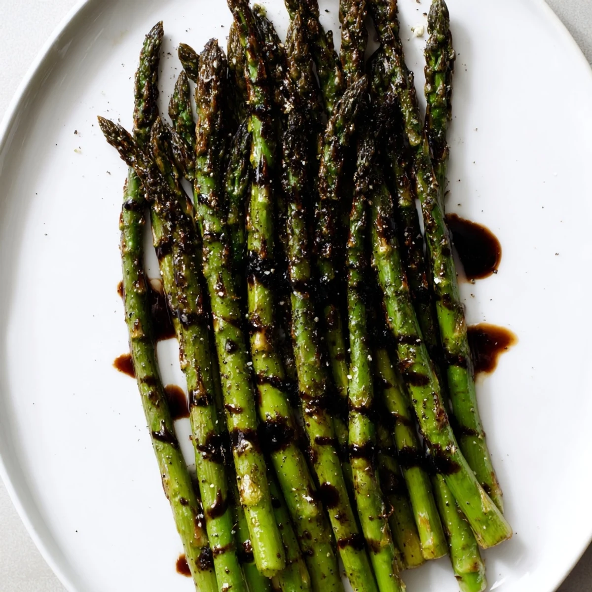 Vibrant green roasted asparagus with balsamic glaze and toasted pine nuts on a rustic wooden board.