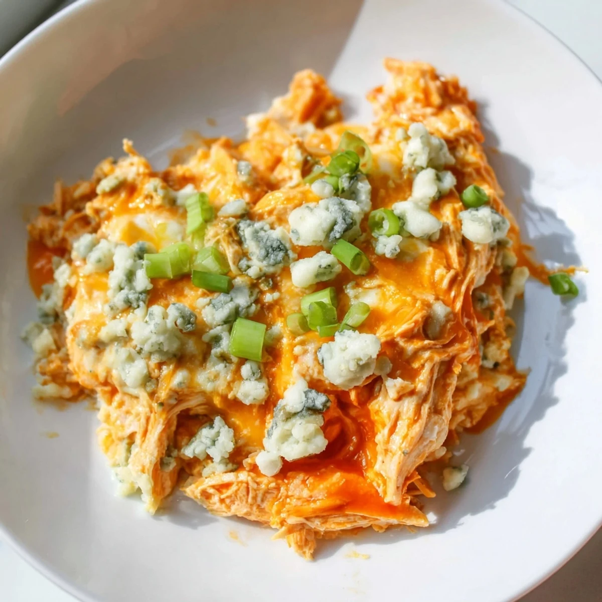 Golden-bubbly Keto Buffalo Chicken Dip topped with green onions and blue cheese crumbles, garnished with celery sticks on the side.