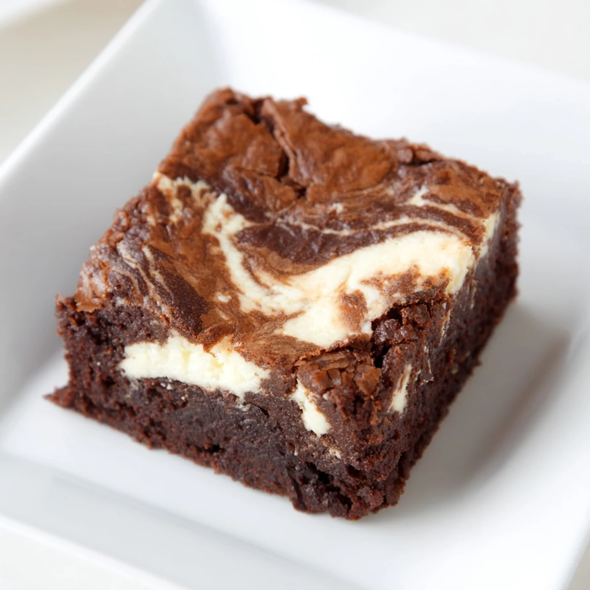 Golden-brown Cottage Cheese Brownies with a visible creamy swirl and glossy top, presented on a white plate for a decadent dessert serving.