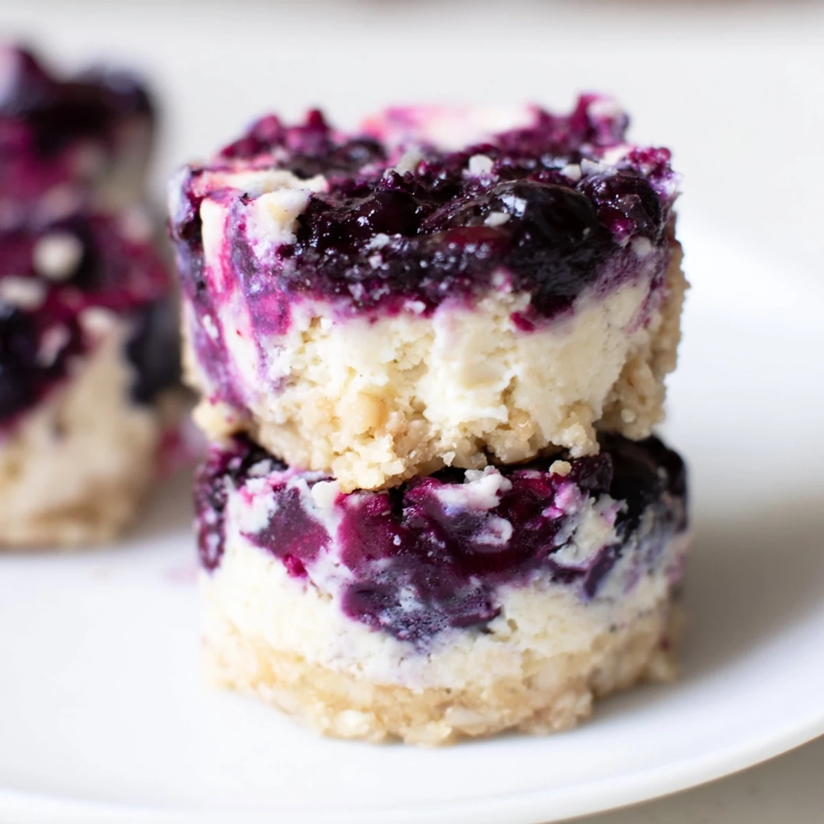 A close-up shot of Blueberry Cheesecake Protein Bites with a spoonful of blueberry compote being added for a vibrant swirl effect.
