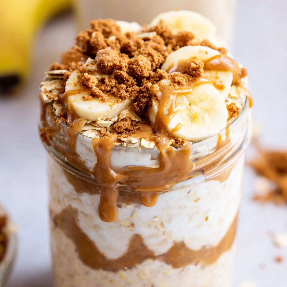 Creamy Quick Biscoff Overnight Oats layered in a jar with crumbled cookies and sliced banana.