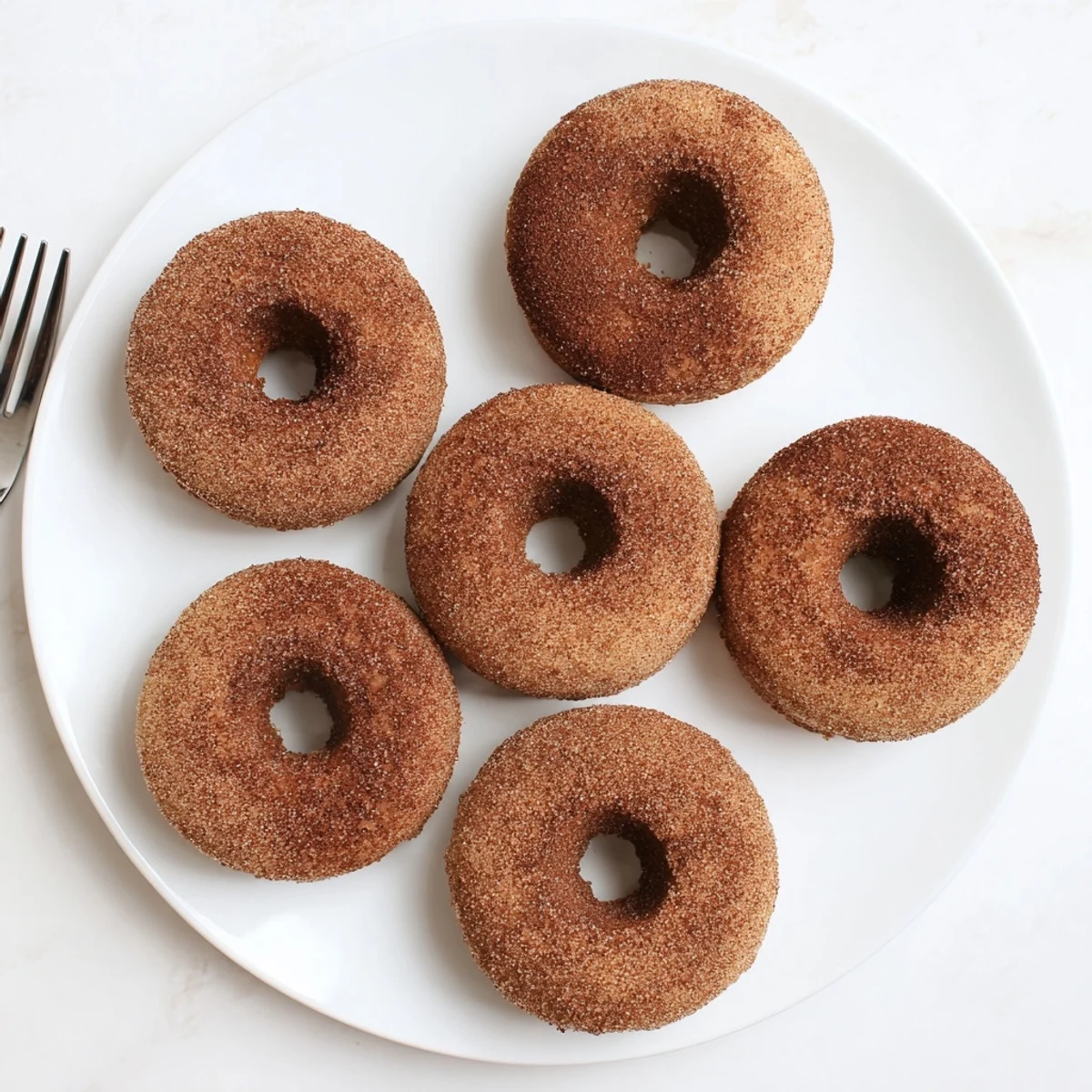 Perfectly baked Delicious Baked Cinnamon Sugar Donuts on a wire rack, cooling after being rolled in cinnamon sugar.