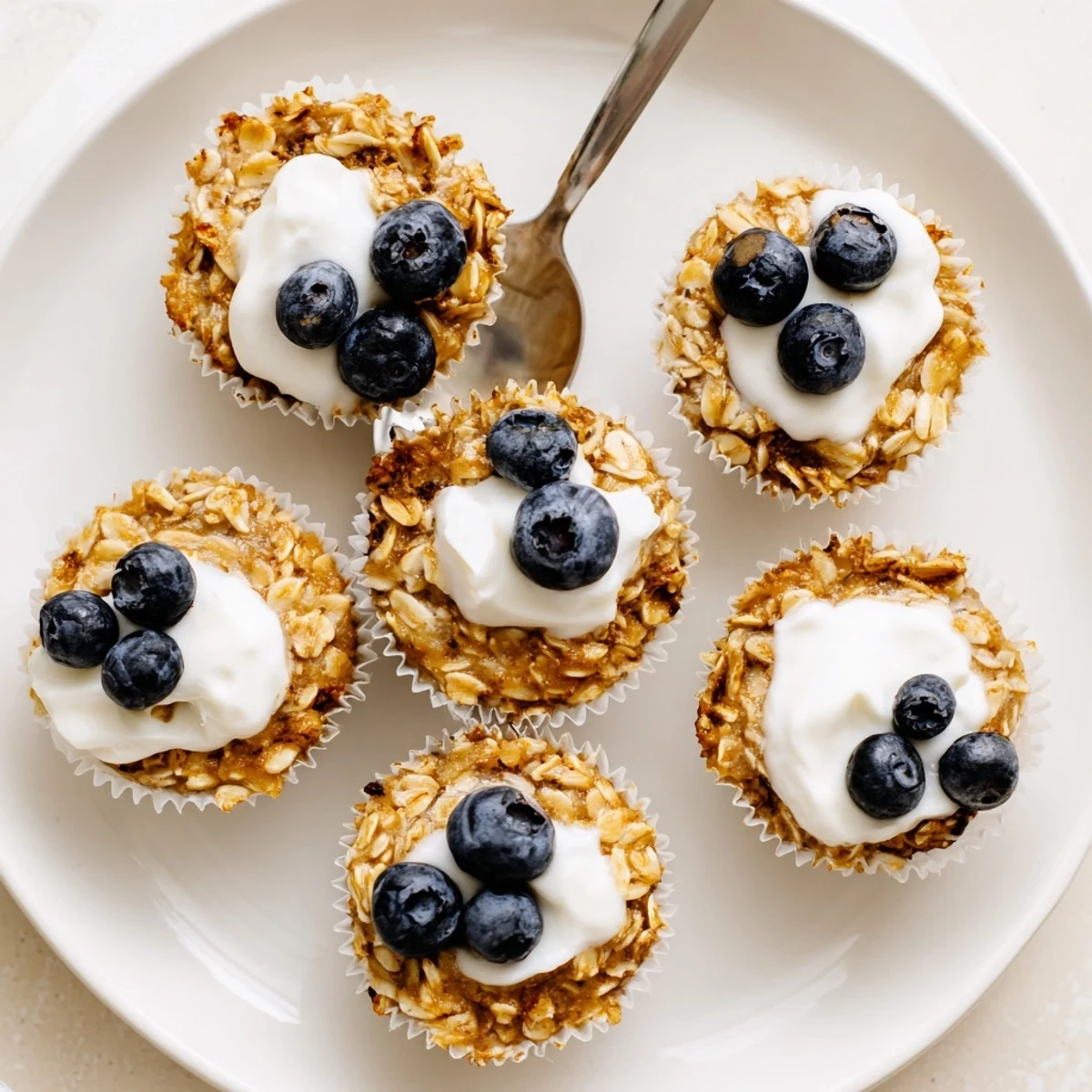 A close-up of Baked Oatmeal Cups with Greek Yogurt shows the soft, moist interior studded with blueberries and a drizzle of honey.