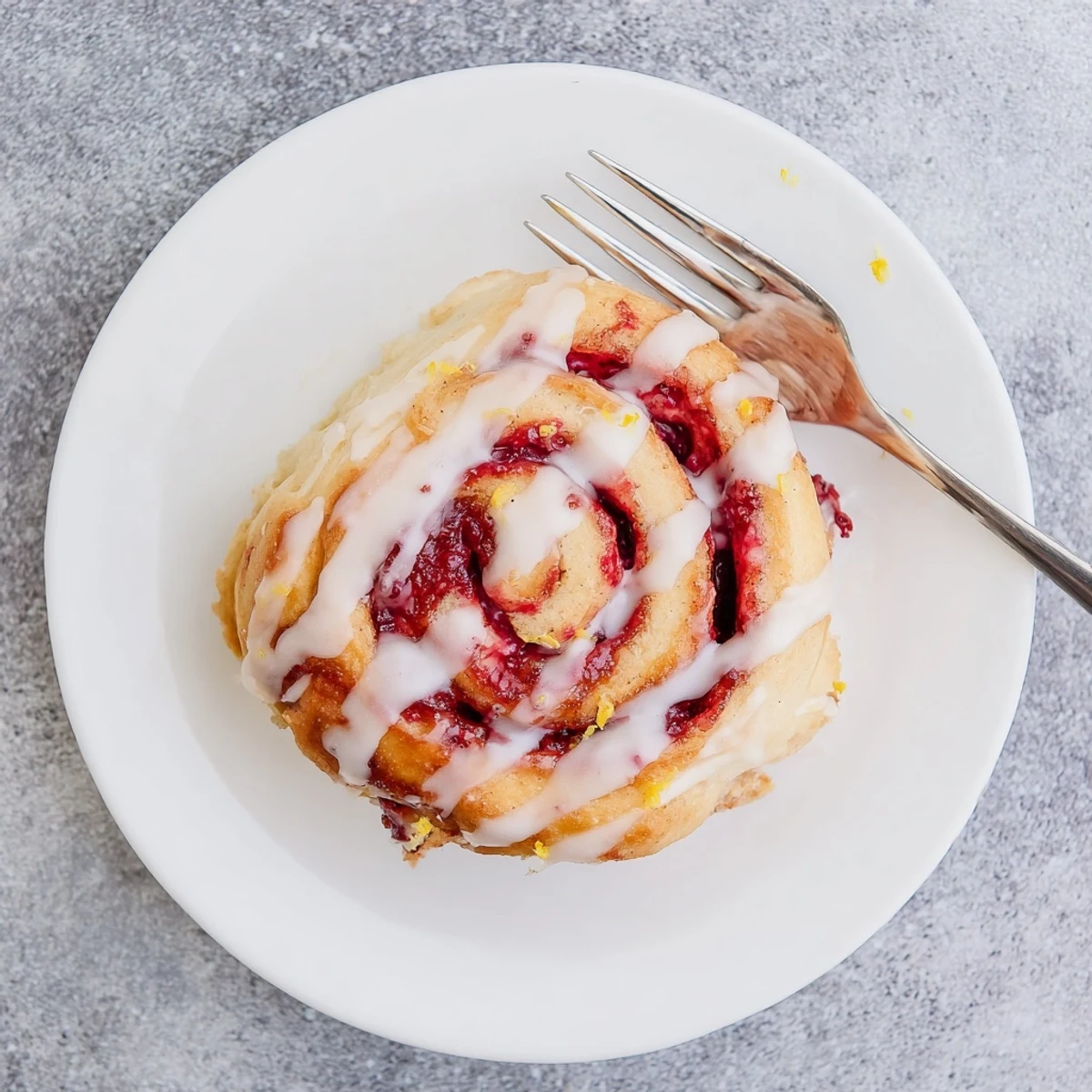 Warm Raspberry Cinnamon Rolls With Lemon Glaze served on a breakfast plate with a cup of coffee.