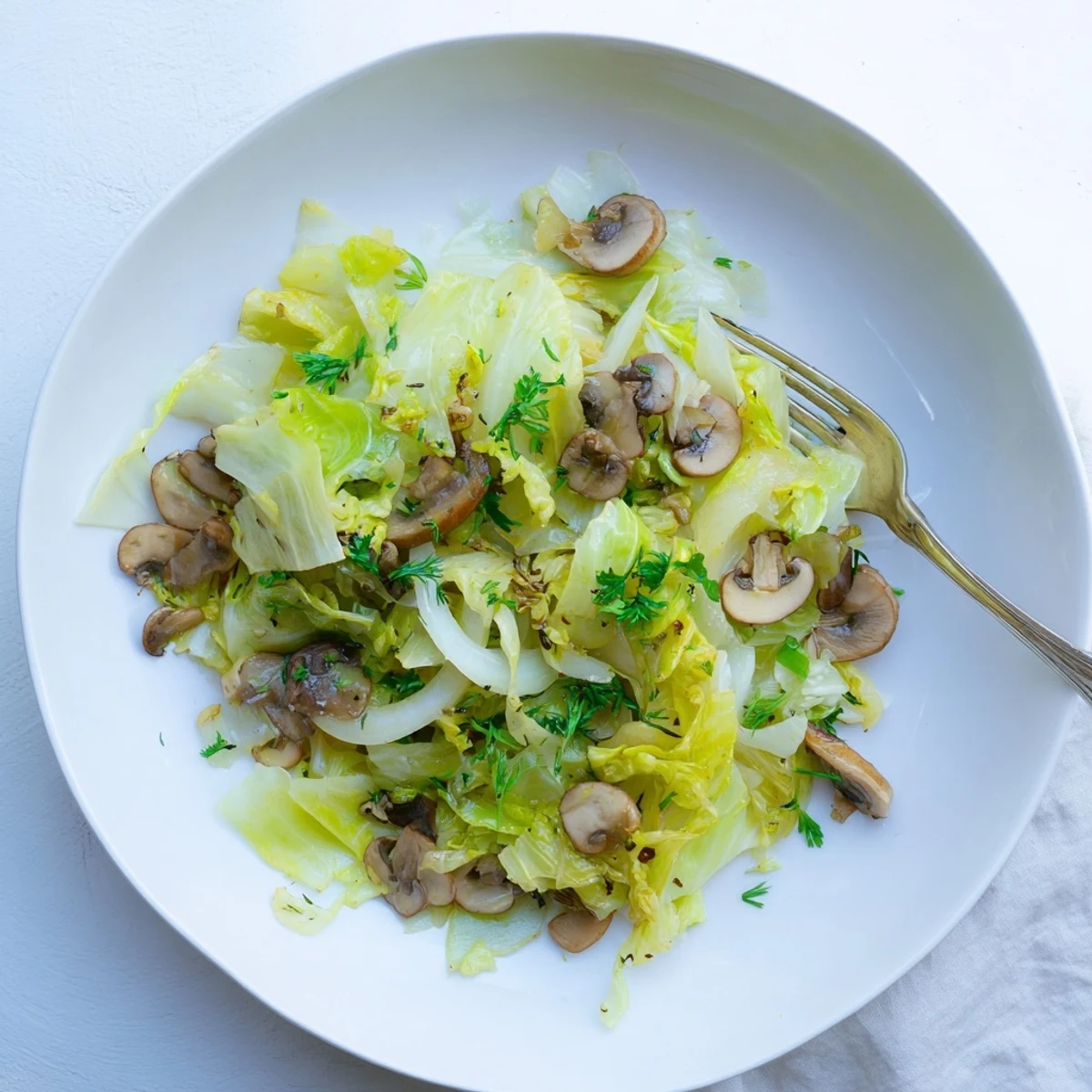 The Vegetarian Cabbage Mushroom Sauté plated on a white ceramic dish with a side of brown rice and lemon wedges on a rustic table.
