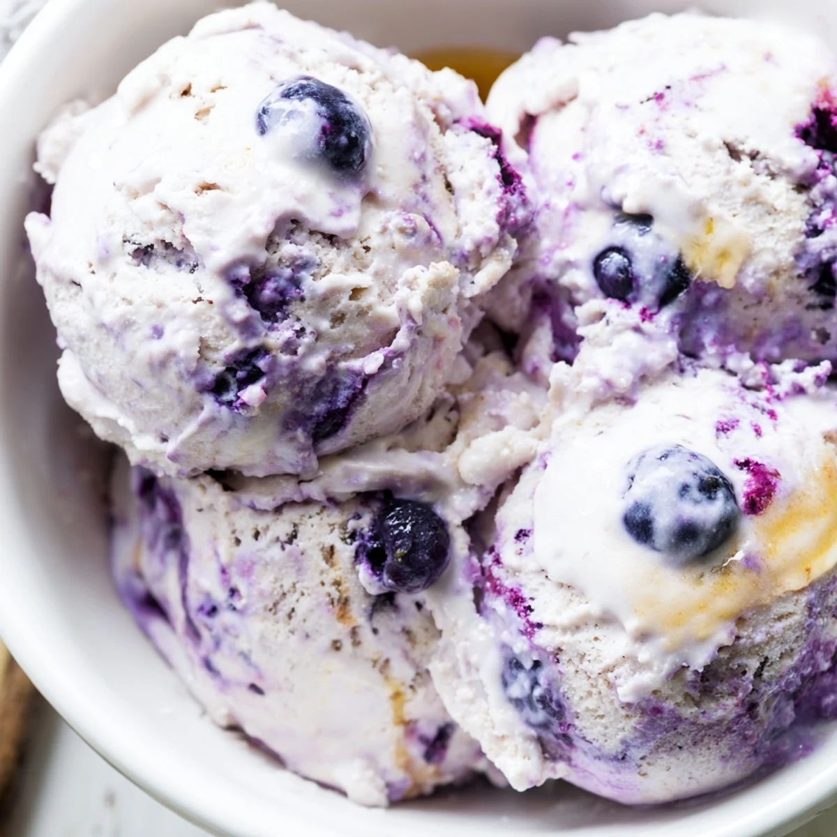 Close-up of Blueberry Cottage Cheese Ice Cream on a spoon, with honey drizzle and a cottage cheese container nearby.