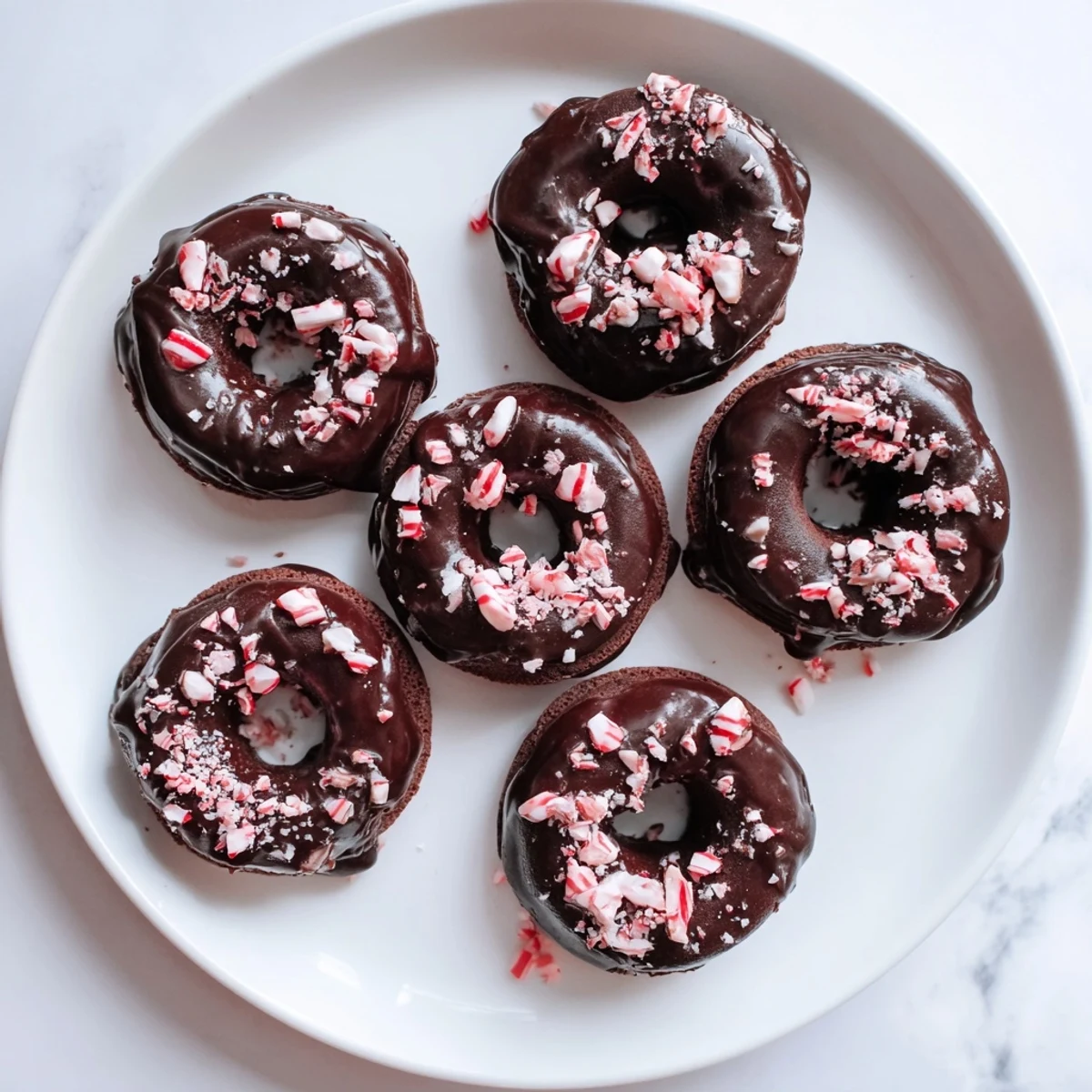 Freshly baked Chocolate Peppermint Mochi Donuts on a white plate, drizzled with glaze and dusted with peppermint crumbs.
