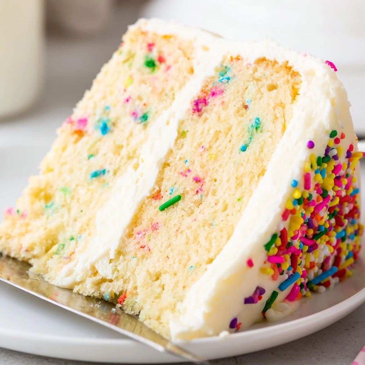 Festive confetti cake slices displaying rainbow sprinkles baked into fluffy vanilla layers with creamy frosting