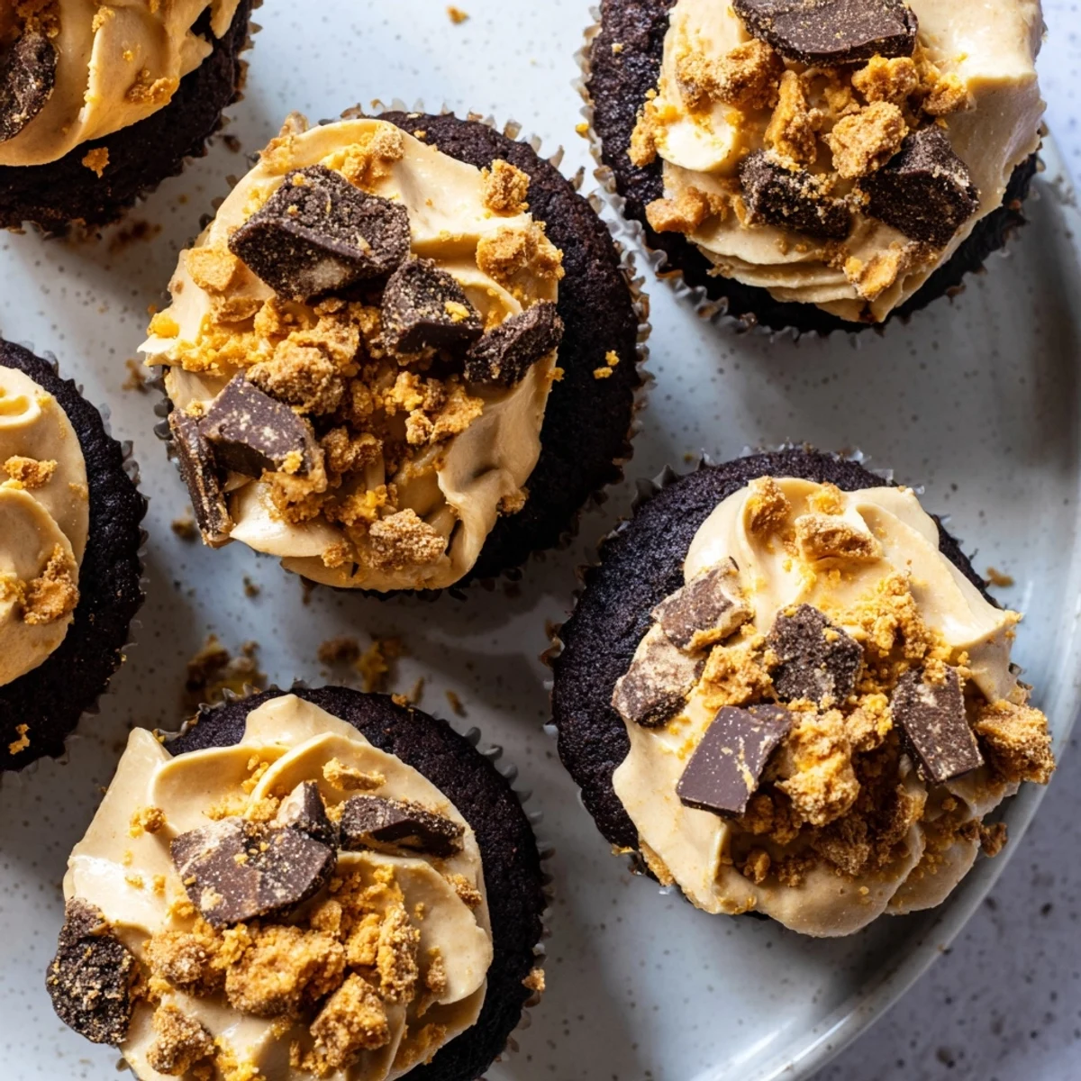 Plate of indulgent Butterfinger cupcakes with fluffy peanut butter frosting and candy pieces