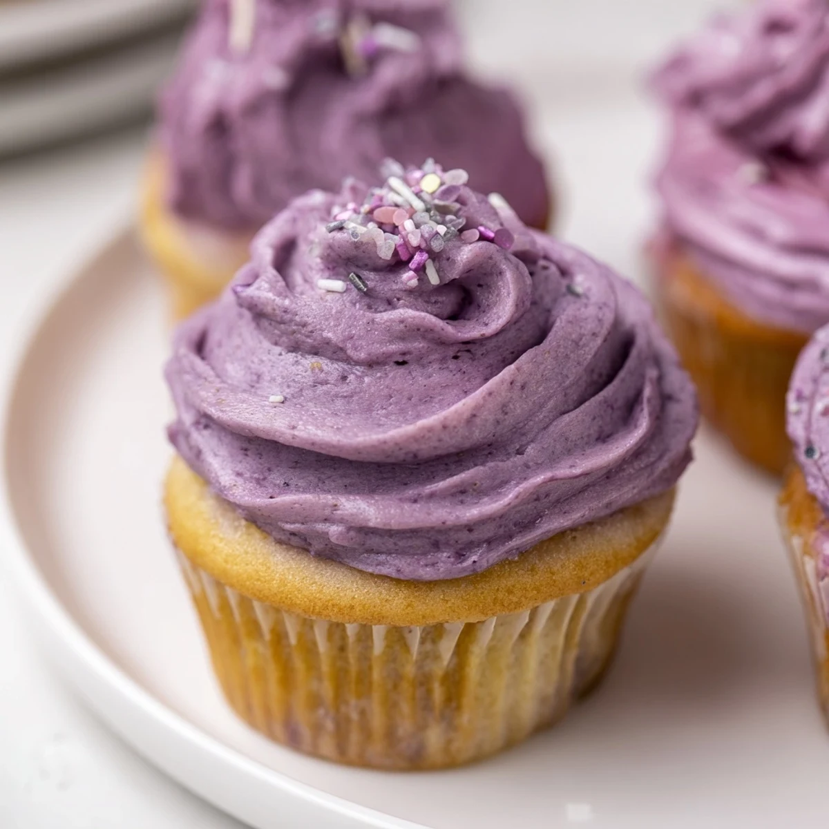 Fluffy purple grape soda cupcakes topped with swirling grape buttercream frosting on a white plate.