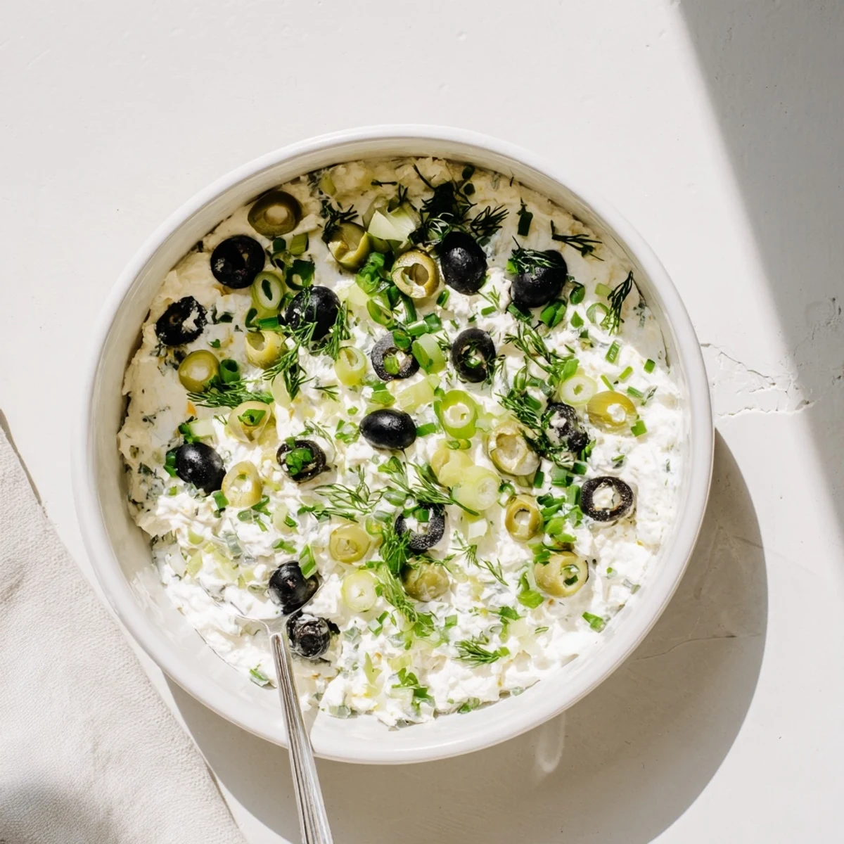 Creamy white appetizer dip speckled with chopped green and black olives served with crispy crackers