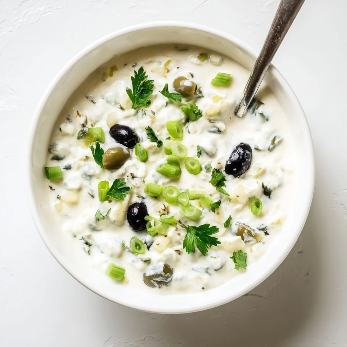 Tangy cream cheese olive dip topped with parsley and green onions in glass serving dish