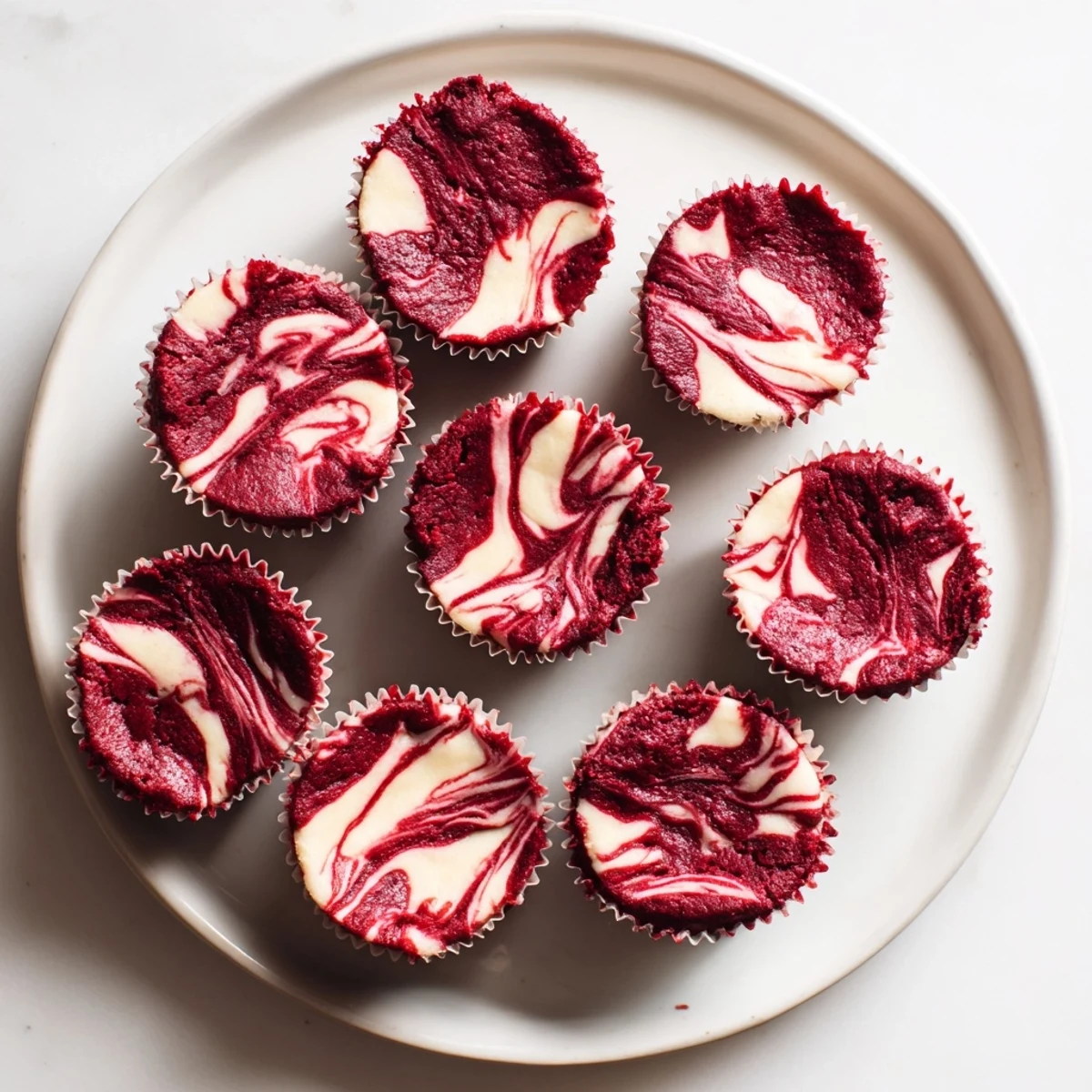 Fudgy red velvet brownie bites topped with swirling cream cheese marble patterns on a white plate