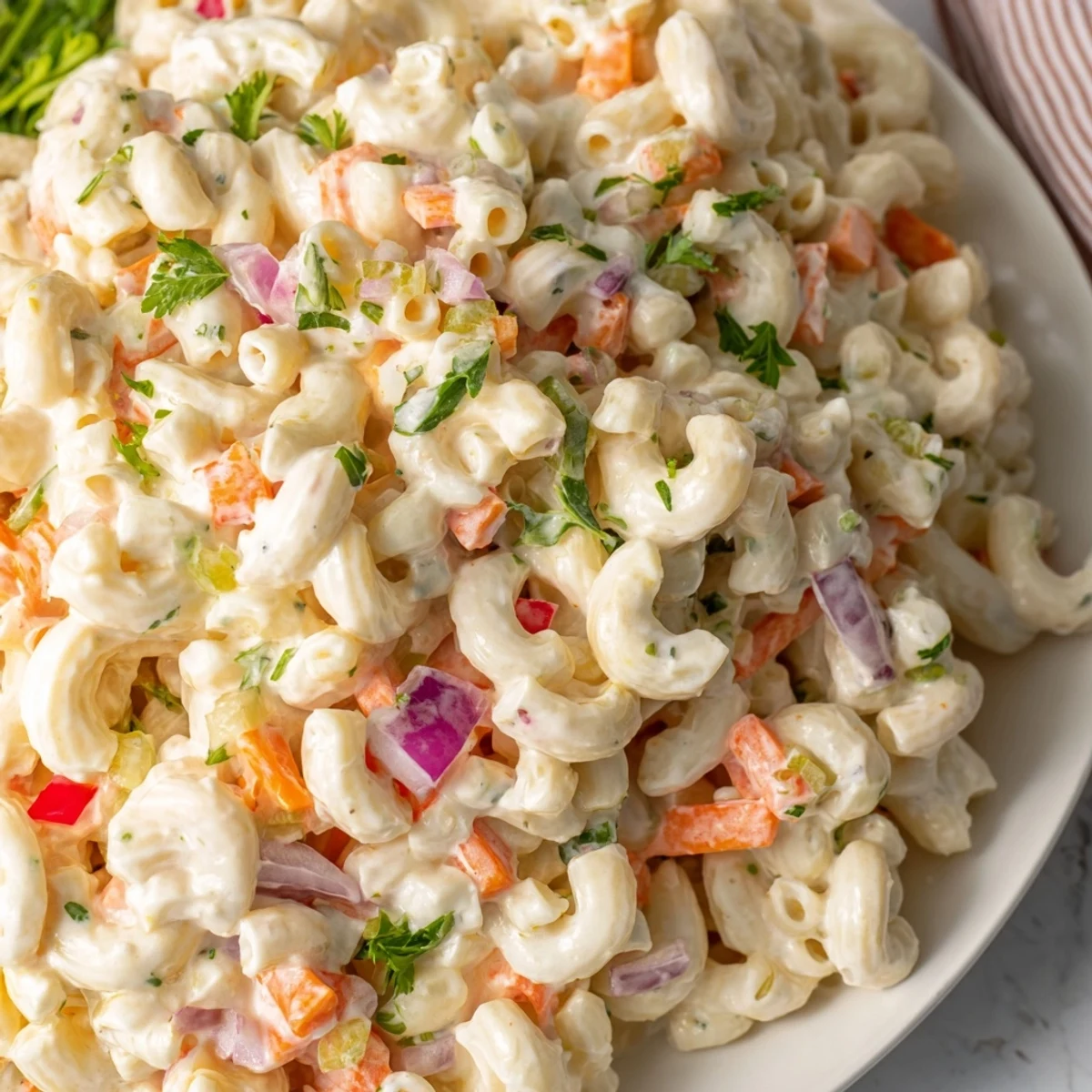 Creamy dressed macaroni salad featuring tender pasta, shredded carrots, and diced red onion