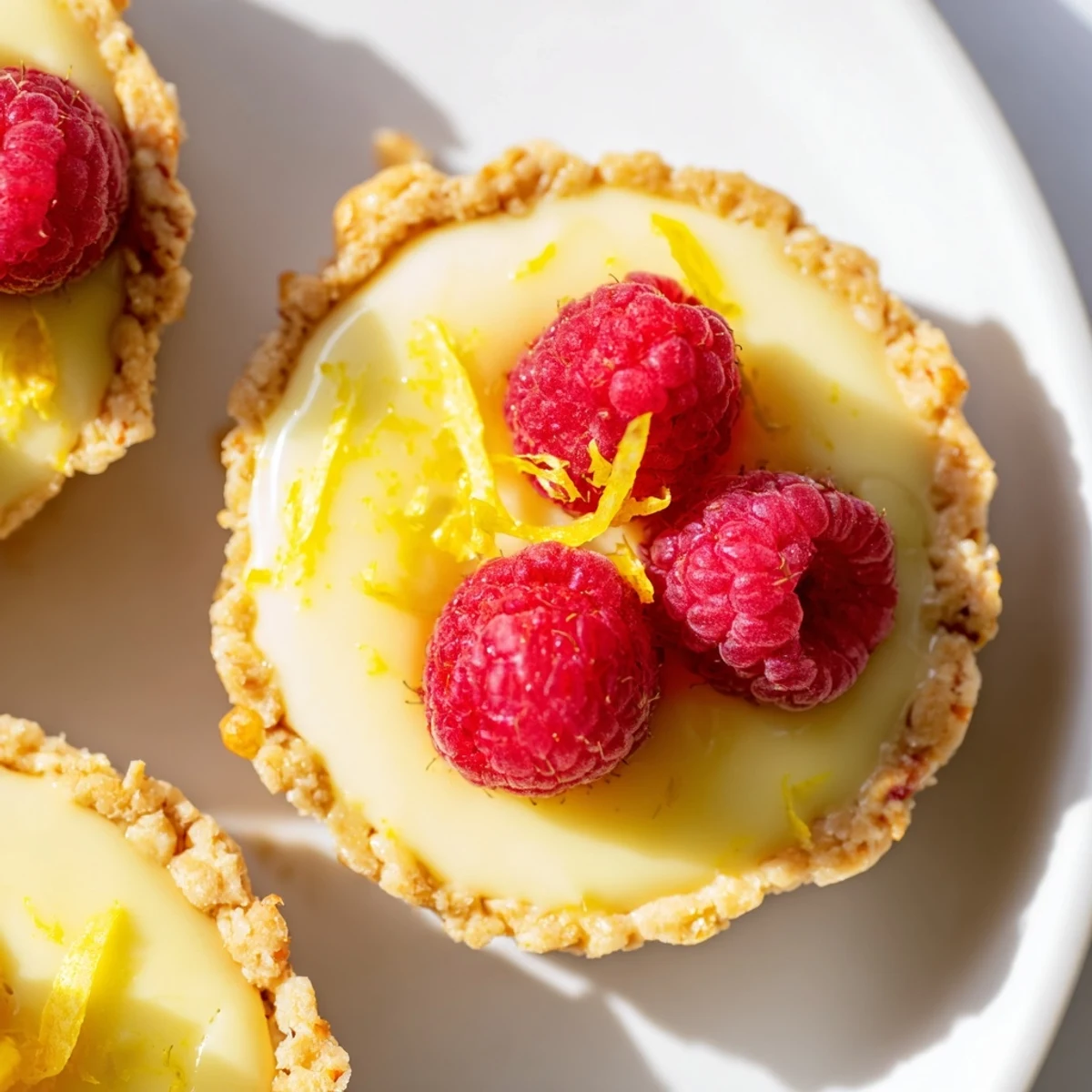 Creamy vegan lemon tarts in crisp almond crusts garnished with delicate lemon zest curls