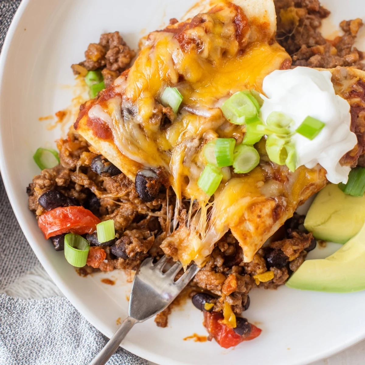 Beef Skillet Enchiladas bubbling with melted cheese, cilantro, and creamy avocado