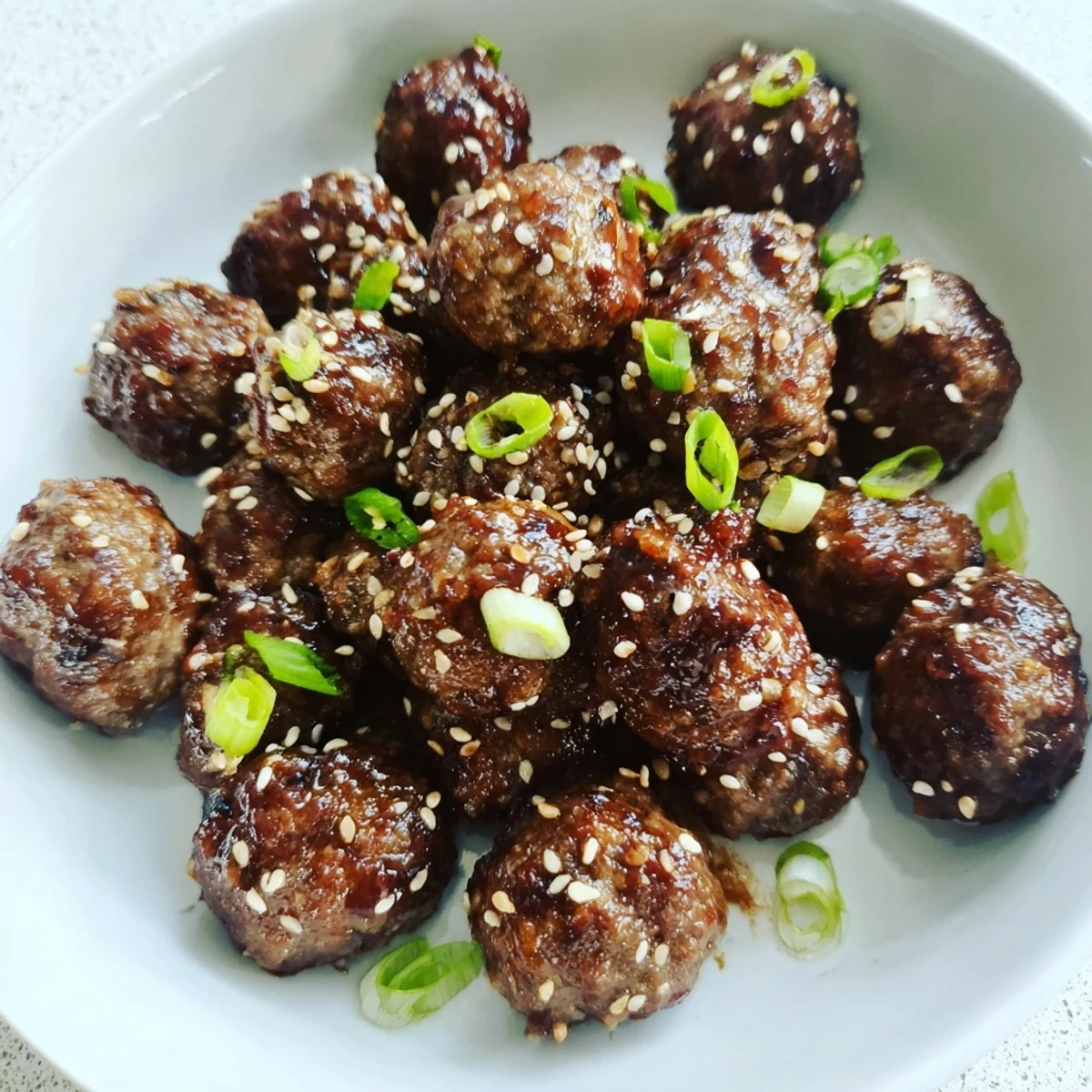 Firecracker Meatballs piled on a platter, glossy spicy sauce, sesame garnish
