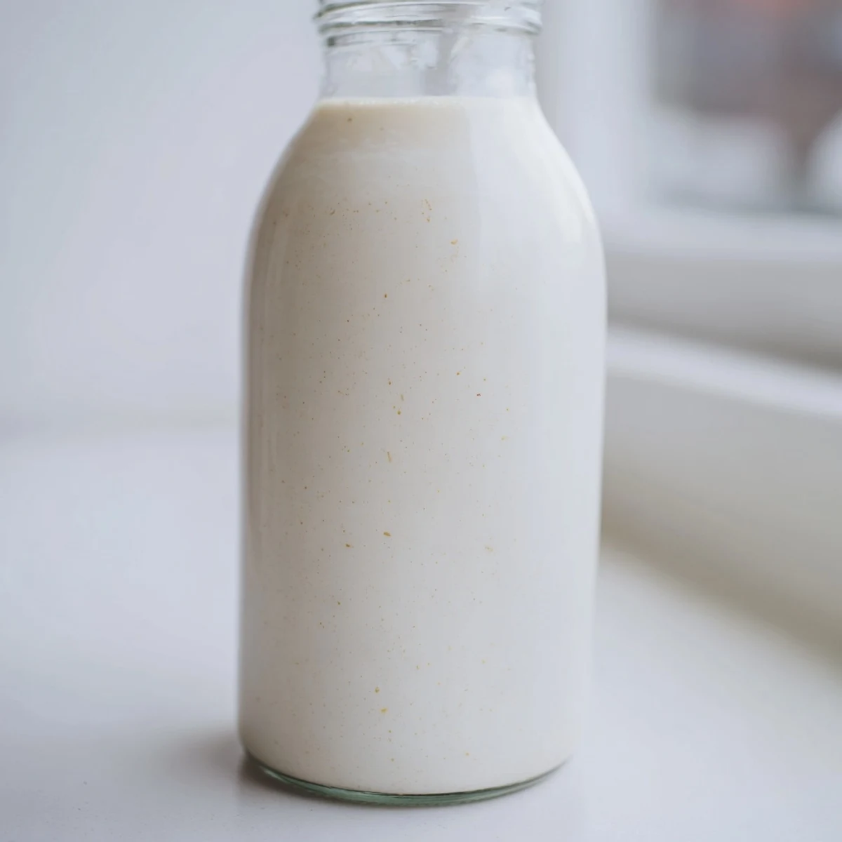 Fresh homemade coconut milk poured into a clear glass jar, showing its creamy white texture