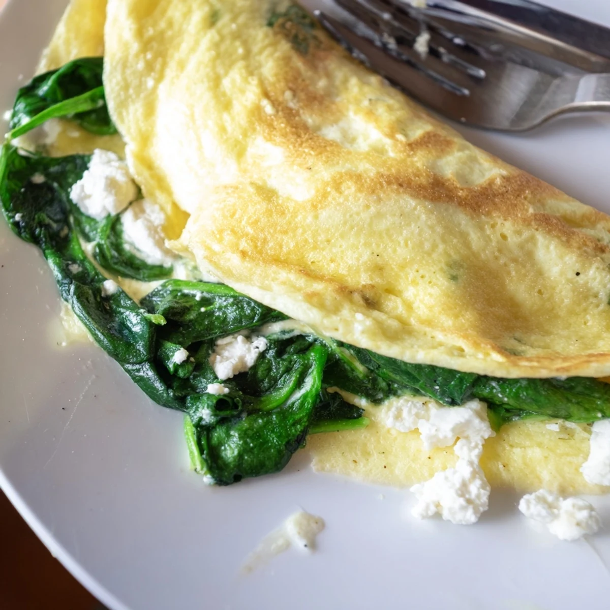 Golden spinach feta omelet recipe folded on a white plate with melty cheese