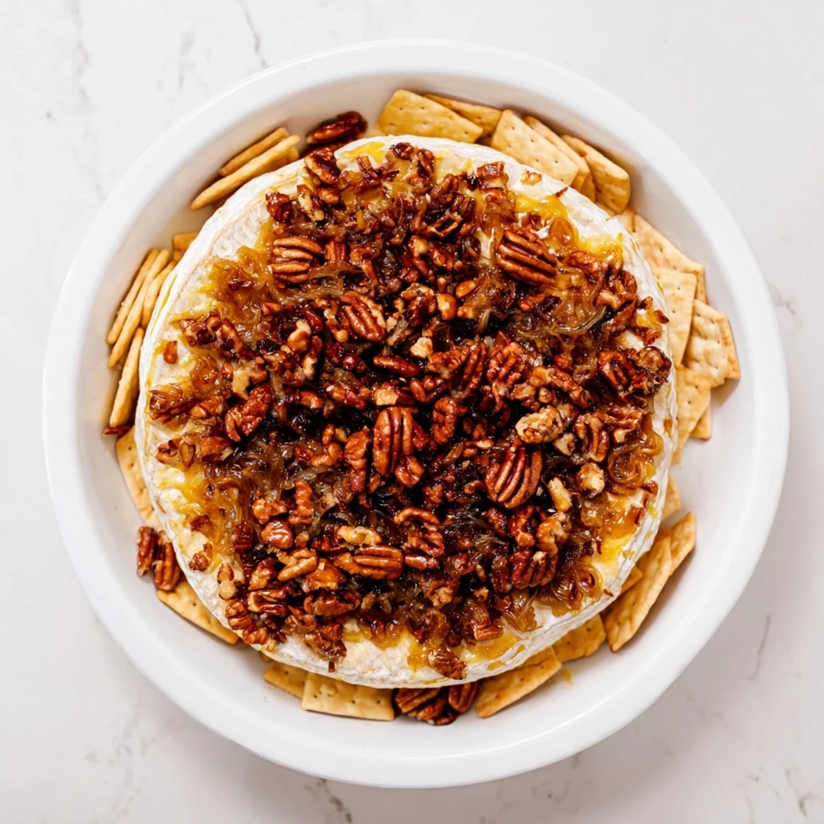 Golden wheel of baked brie with caramelized onions and toasted pecans oozing on a wooden board