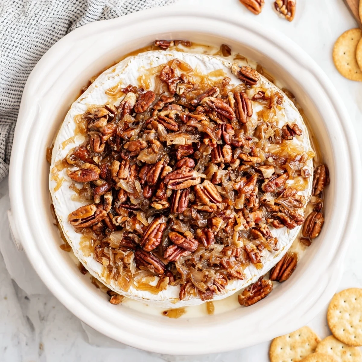 Warm French baked brie melting beneath caramelized onions and pecan halves on a rustic platter