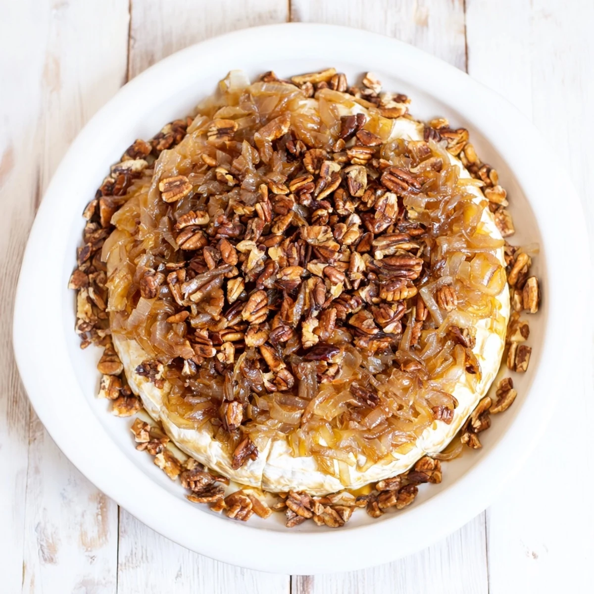 Creamy baked brie topped with sweet onions and crunchy pecans served with crackers for dipping