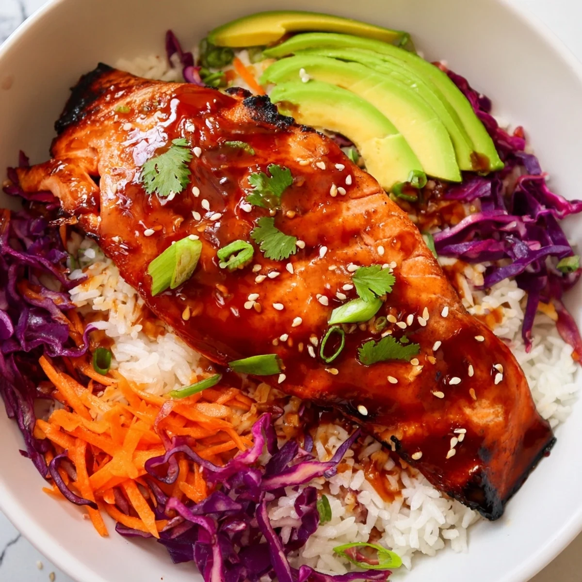 Caramelized sriracha honey glazed salmon bowls topped with avocado, sesame seeds, and fresh cilantro