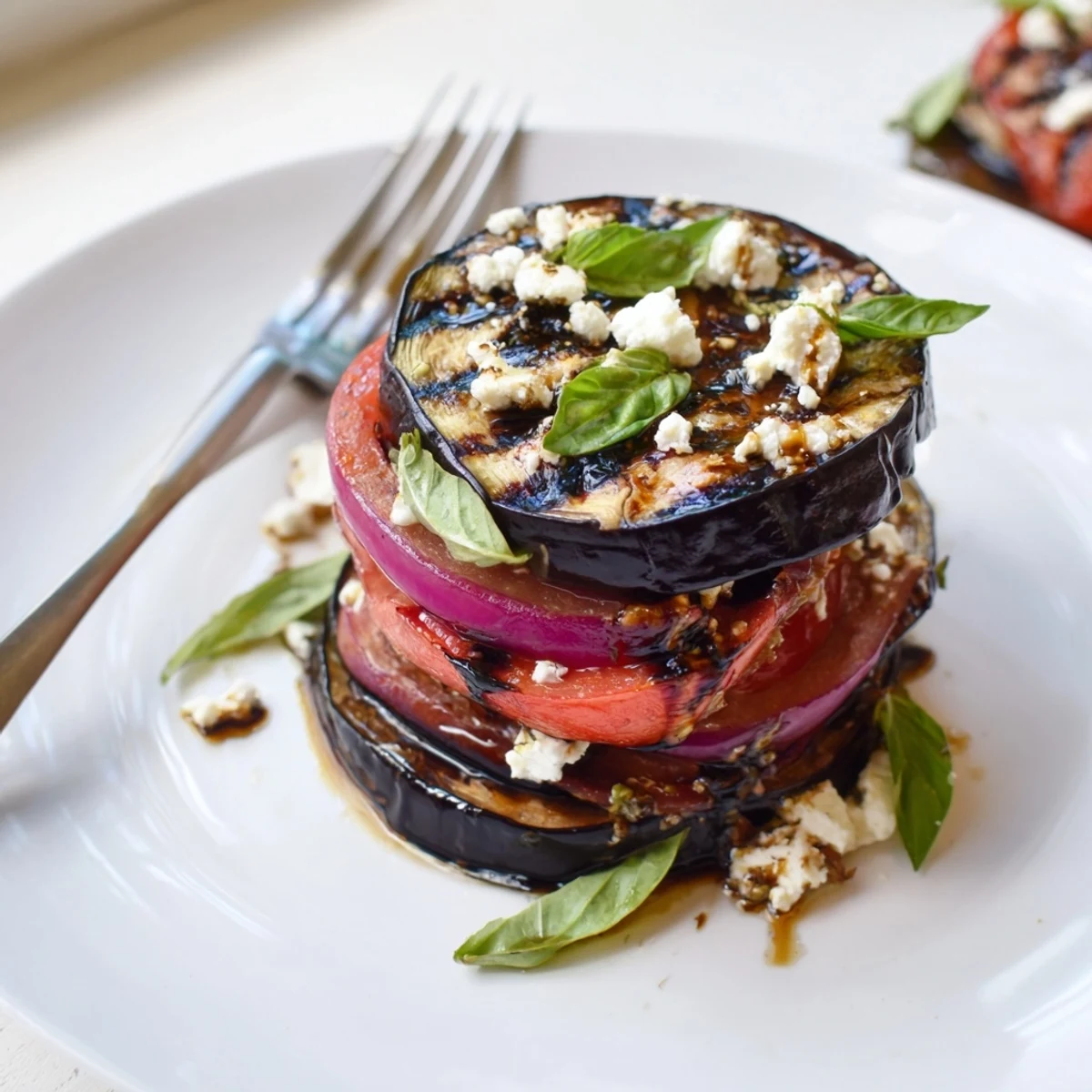Smoky grilled tomato eggplant stacked on a platter with crumbled feta and fresh basil