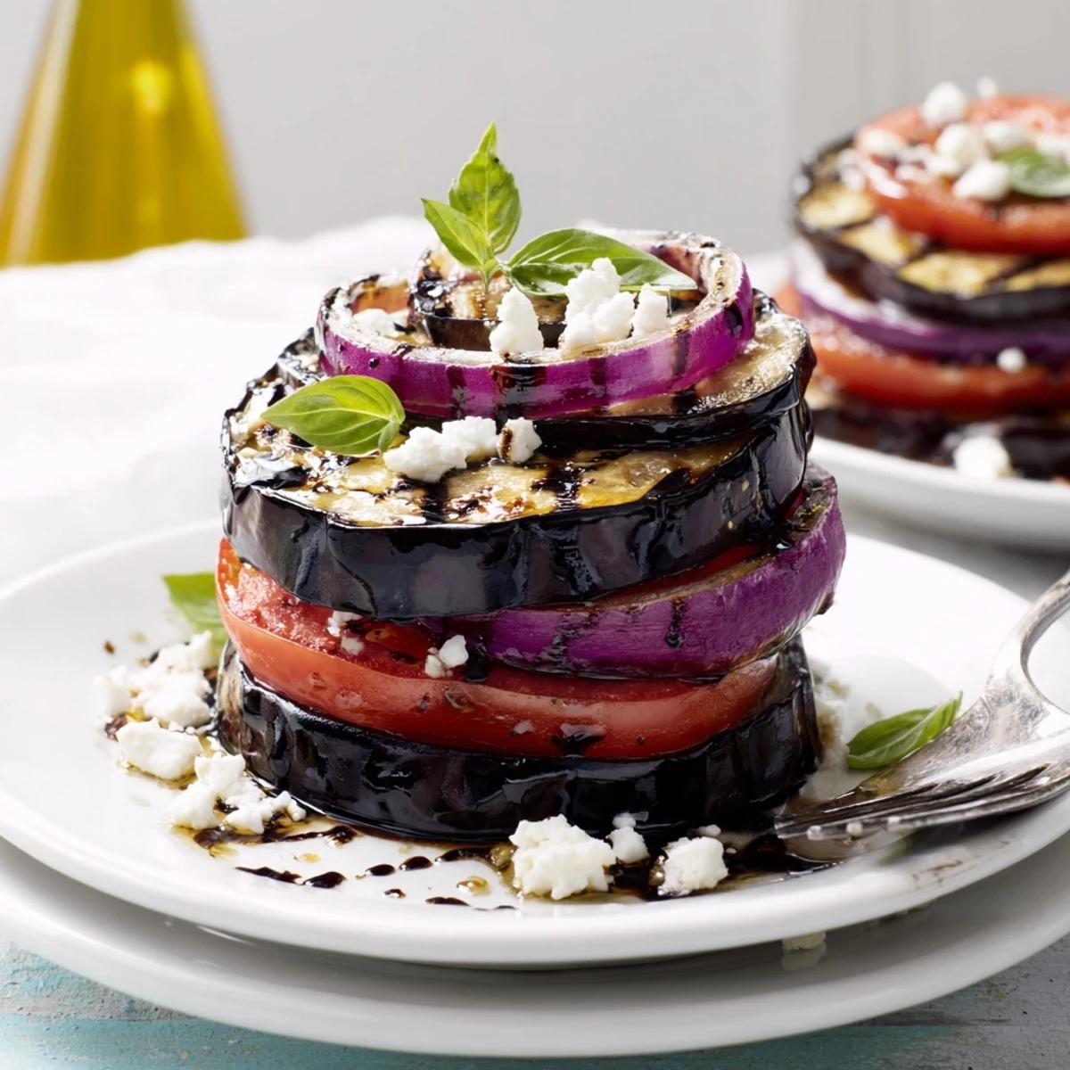 Vibrant grilled tomato eggplant layered with red onion and herbs ready for a summer dinner