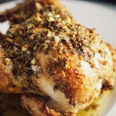 A succulent BBQ Roast Lemon and Oregano Chicken garnished with fresh oregano sprigs, sliced lemons, and ready to serve for dinner.