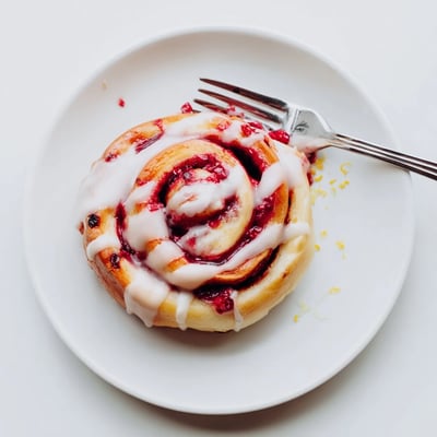 Golden Raspberry Cinnamon Rolls With Lemon Glaze drizzled with icing on a rustic wooden table.
