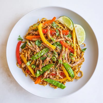Sweet Chilli Turkey Noodle Stir Fry served hot with sesame seeds and coriander garnish on a wooden table.