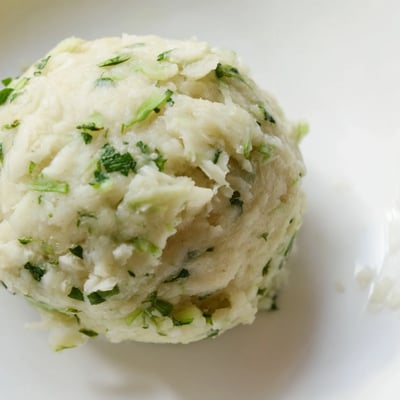 Close-up of round German Cabbage Dumplings garnished with parsley, ready to be served with a creamy mushroom sauce.
