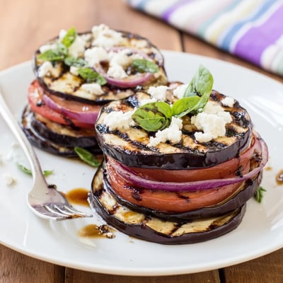 Golden charred eggplant and juicy grilled tomato slices drizzled with balsamic marinade on a rustic plate