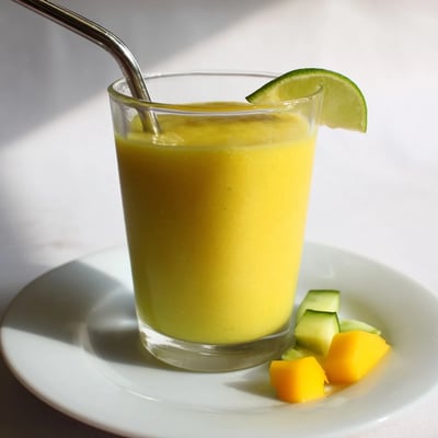 Bright yellow mango cucumber smoothie blended smooth and served over ice cubes